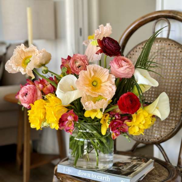 Colorful bouquet in a clear glass vase with poppies, ranunculus, calla lilies, and yellow blooms