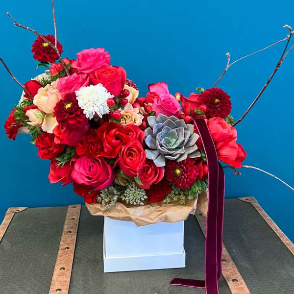 Bright red and pink floral arrangement with roses and a succulent in a white box