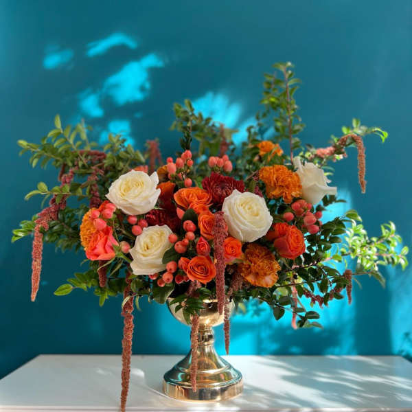 Mixed orange and white floral arrangement in a gold vase