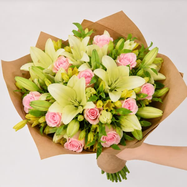 Bouquet of pink roses and pale lilies wrapped in brown paper