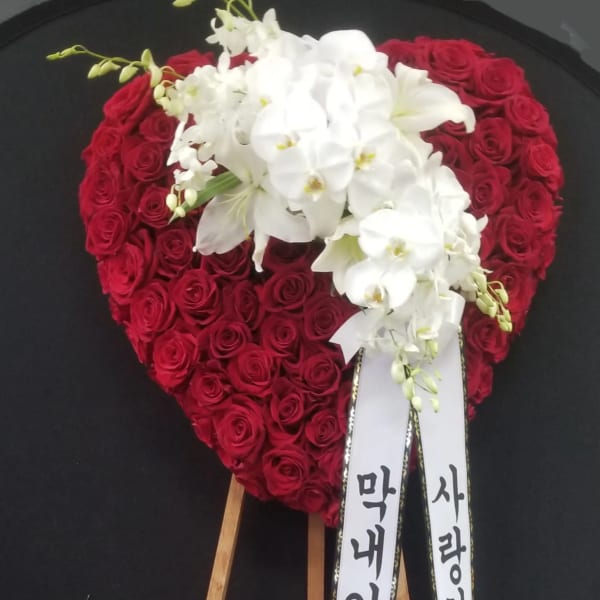 Heart-shaped red rose wreath with white orchids on a wooden stand