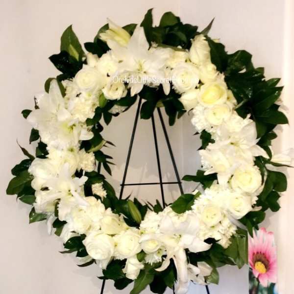 White floral wreath on a black stand with dark green leaves