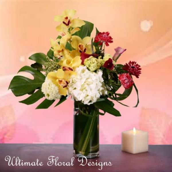 Mixed bouquet of yellow orchids, white hydrangea, and red flowers in a tall glass vase