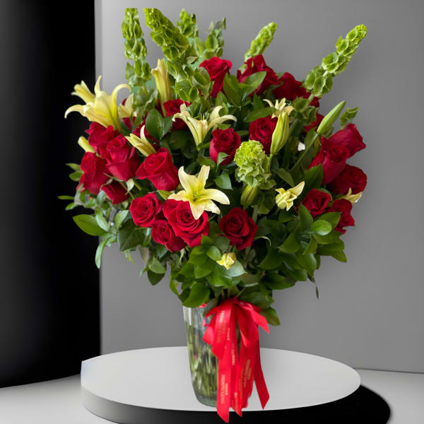 Bouquet of red roses and pale lilies in a glass vase with a red ribbon