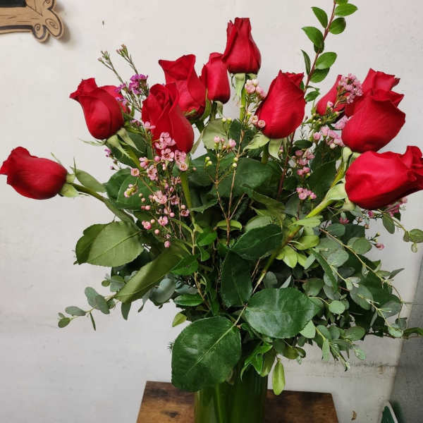 Bouquet of red roses with pink filler flowers in a green glass vase
