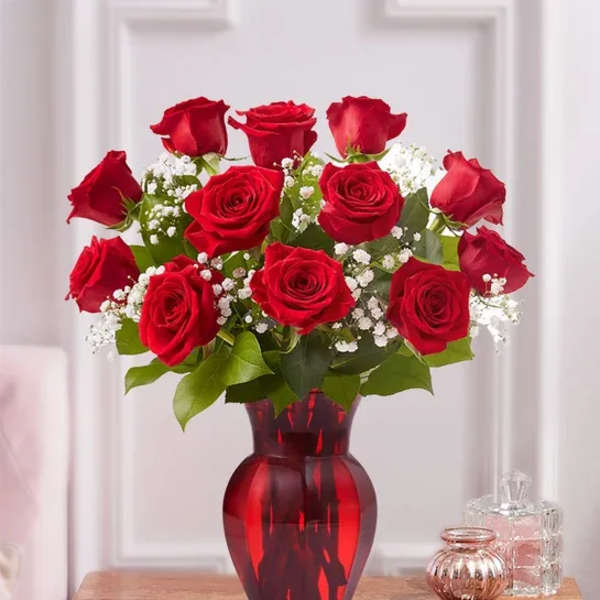 Red roses arranged in a red glass vase with white filler flowers