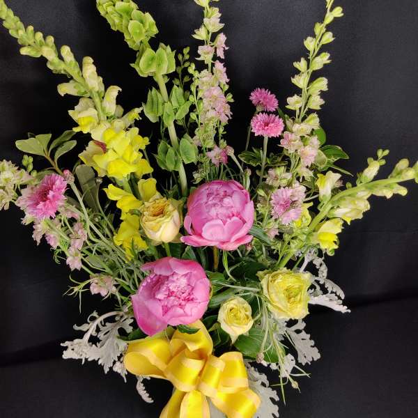 Pink peonies and yellow flowers in a vase with a yellow ribbon