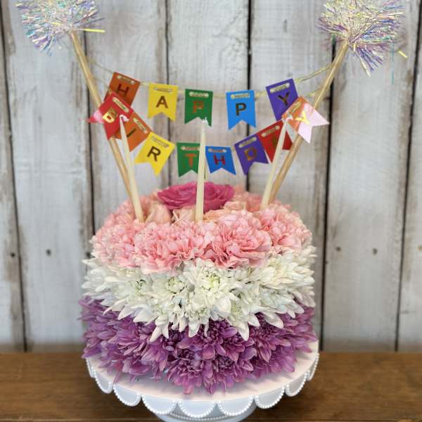 Birthday cake made of pink, white, and purple flowers with a banner topper