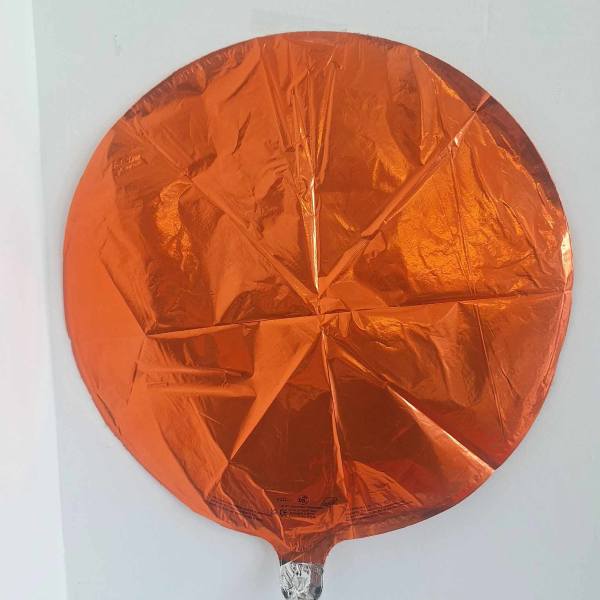 Orange round foil balloon against a white wall