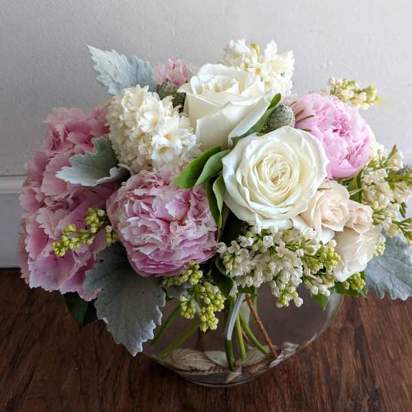 Pink and white bouquet of roses, peonies, and small white flowers in a glass vase