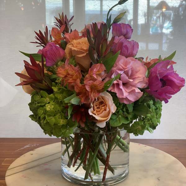Mixed bouquet of pink, peach, and orange flowers in a clear glass vase