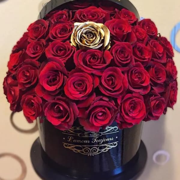 Round black hatbox filled with red roses and a single gold rose in the center