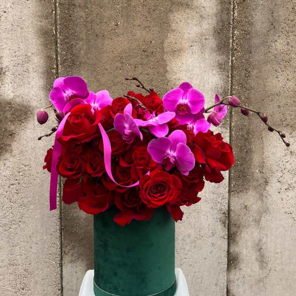 Red roses and pink orchids in a green hatbox