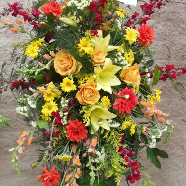 Tall standing spray of mixed flowers in yellow, orange, red, and white