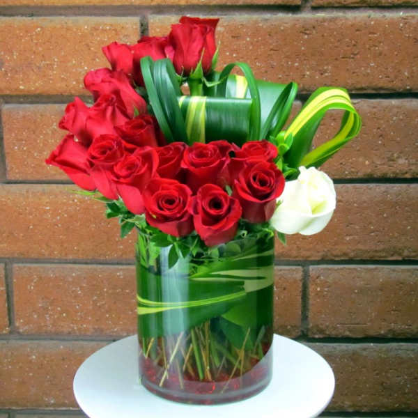Red roses arranged in a glass vase with green ribbon accents