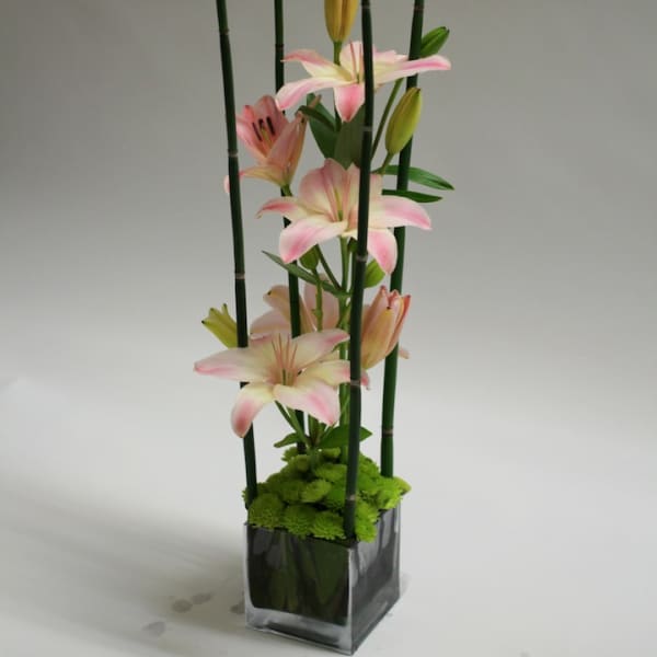 Pink lilies in a tall glass vase with bamboo supports