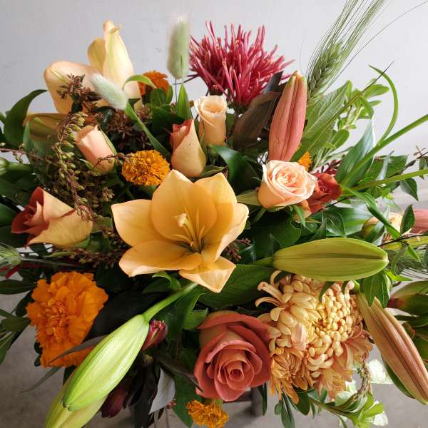 Warm-toned arrangement of peach lilies, roses, marigolds, and mums with buds and textural accents