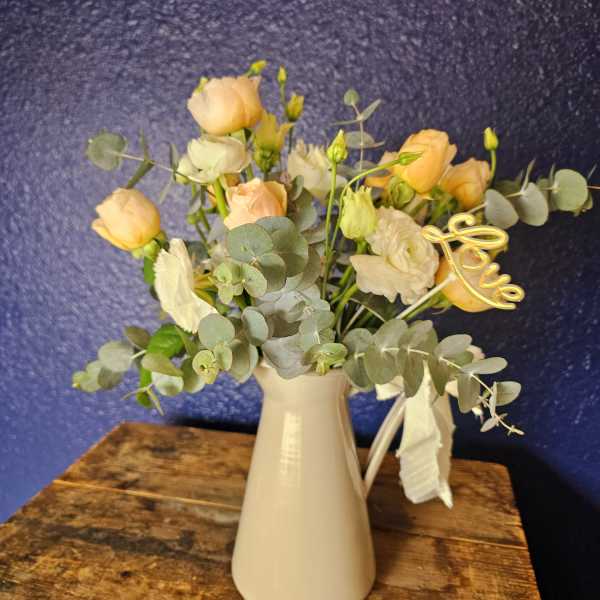 Peach and white flowers in a white vase with eucalyptus and a gold "love" pick