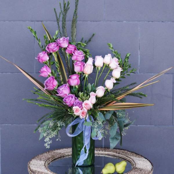 Pink and white roses in a tall green vase with ribbon
