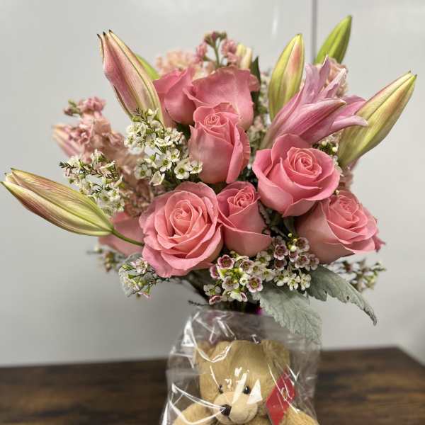 Pink roses and lilies in a wrapped bouquet with a teddy bear