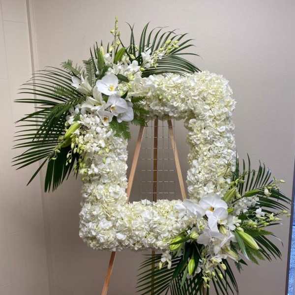 Large white floral wreath on an easel with palm fronds and orchids