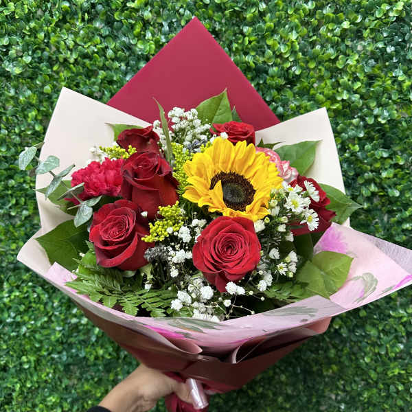 Bouquet of red roses and a sunflower wrapped in pink and cream paper