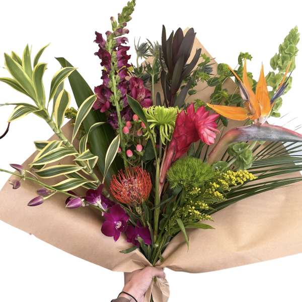 Tropical bouquet with orchids, bird of paradise, and snapdragons wrapped in kraft paper