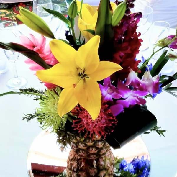 Tropical flower arrangement in a pineapple vase with yellow lilies and purple orchids