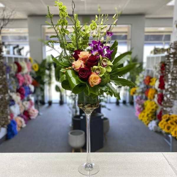 Tall floral arrangement in a clear stemmed vase with roses and orchids