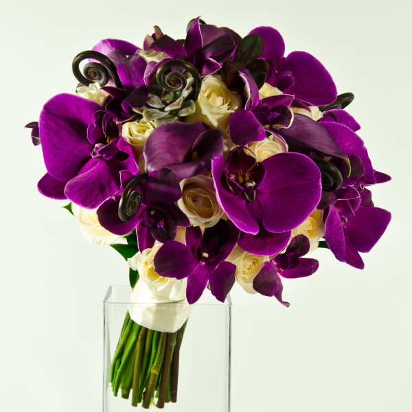 Purple orchids and cream roses in a clear glass vase