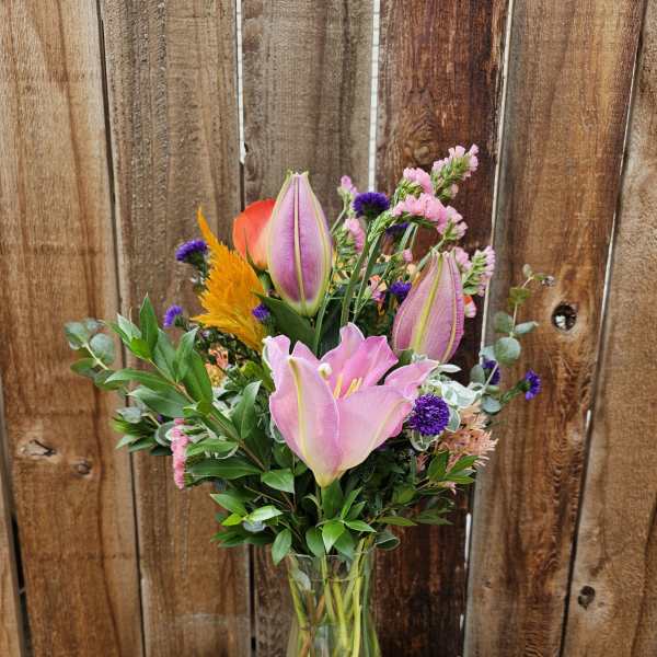 Pink lilies and mixed flowers arranged in a clear glass vase