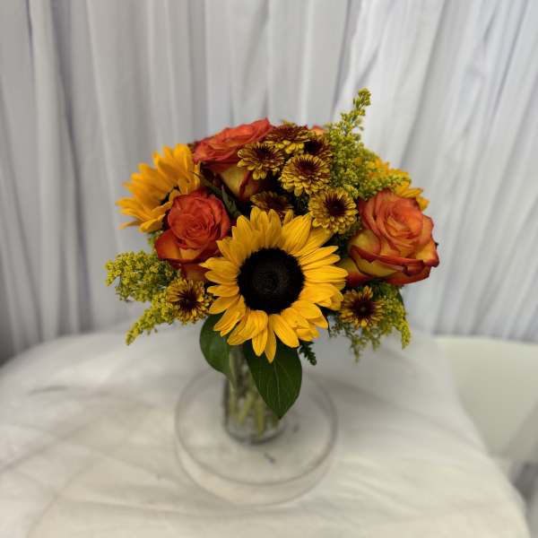 Bouquet of sunflowers, orange roses, and yellow mums in a glass vase