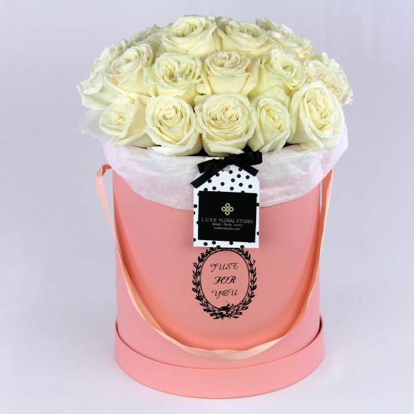 Cream roses arranged in a pink hat box with a ribbon tag