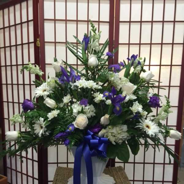 White and purple floral arrangement in a white vase with a blue ribbon