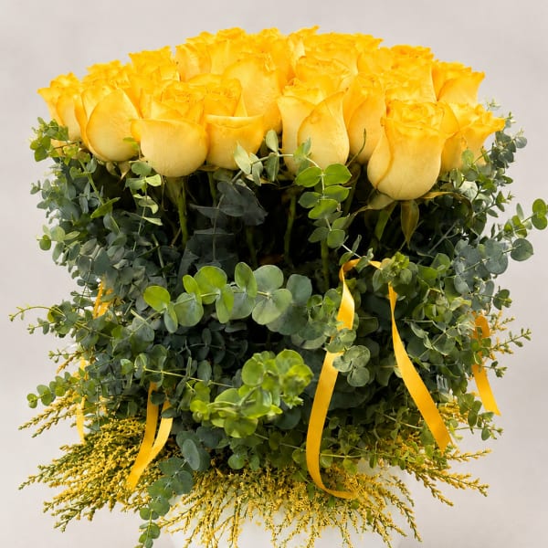 Yellow roses in a white vase with eucalyptus and yellow ribbon