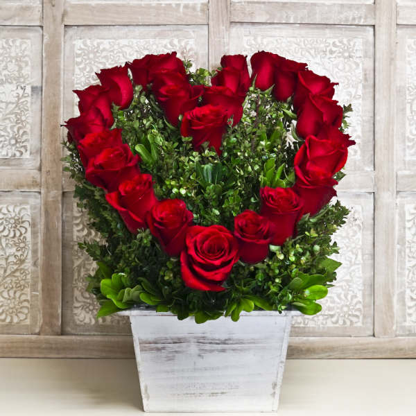 Heart-shaped red rose arrangement in a white wooden planter