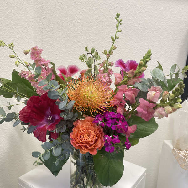 Bright mixed arrangement of orange and pink blooms in a clear glass vase