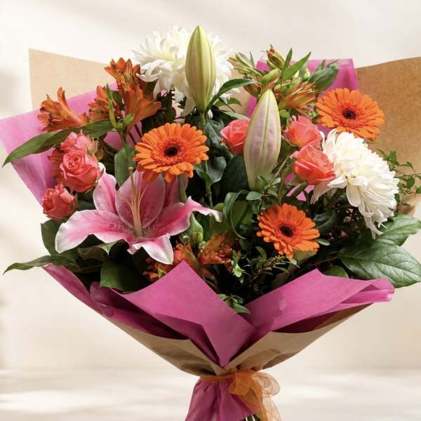 Bouquet of pink lilies, orange gerberas, roses, and white chrysanthemums wrapped in pink paper