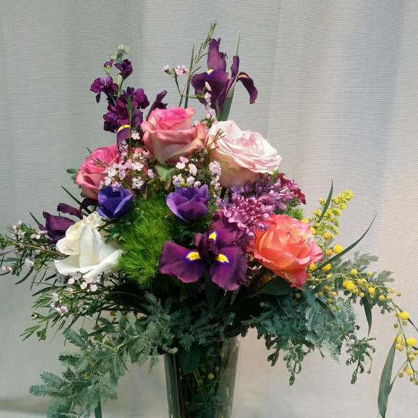 Tall mixed bouquet of roses and purple iris in a clear glass vase