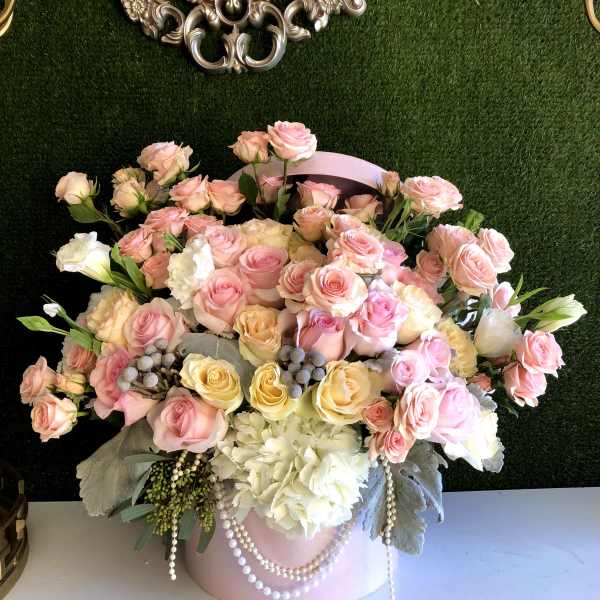 Large pastel arrangement of pink and yellow roses with white hydrangeas in a pink hatbox with pearls
