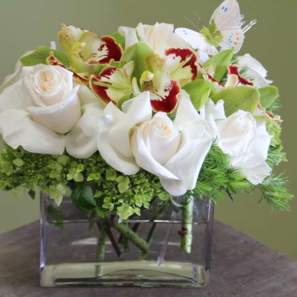 White roses and green orchids in a clear square vase