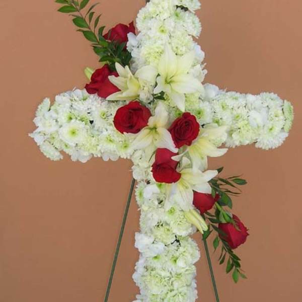 Cross-shaped floral tribute with white flowers and red roses on a stand
