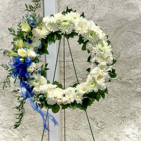 White floral wreath on a stand with blue ribbon accents