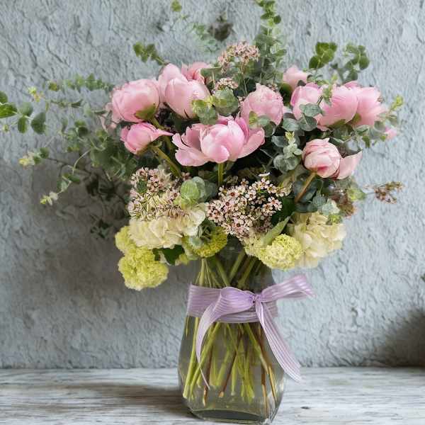 Pink and cream flowers in a glass vase with a lavender ribbon