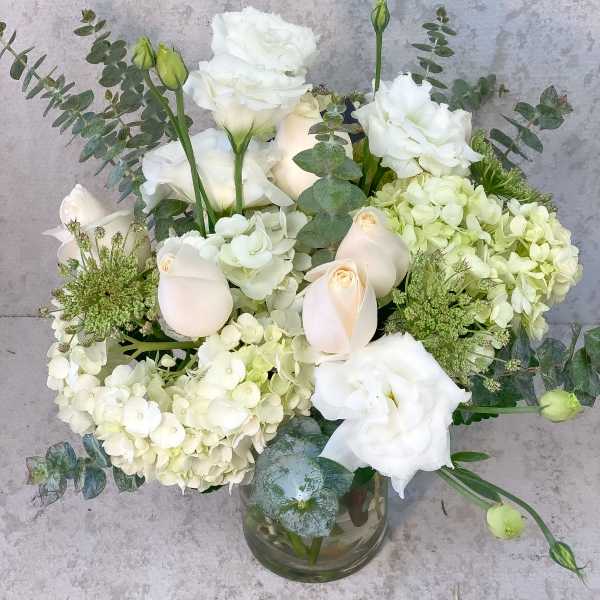 White floral arrangement in a glass vase with hydrangeas and roses