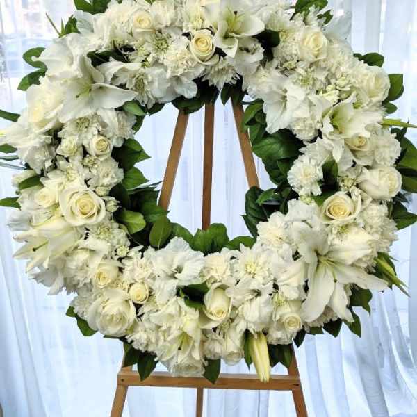 White floral wreath on a wooden easel with roses and lilies