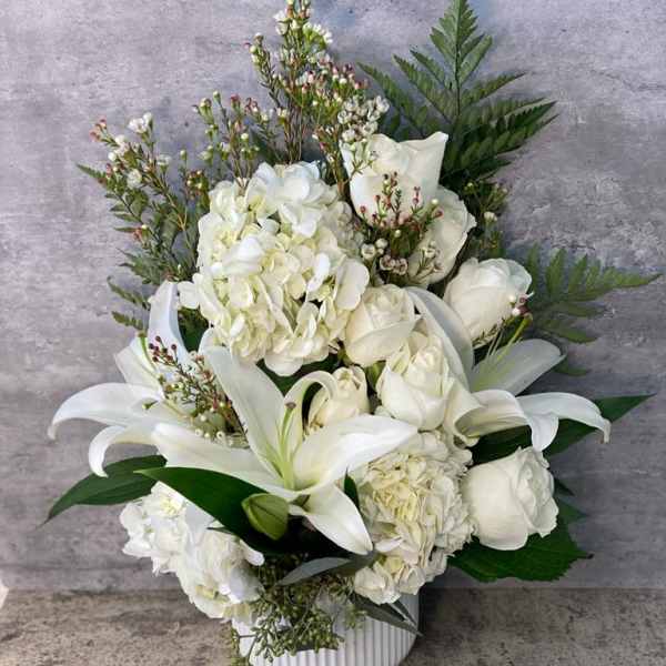White floral arrangement with lilies, roses, and hydrangeas in a white vase