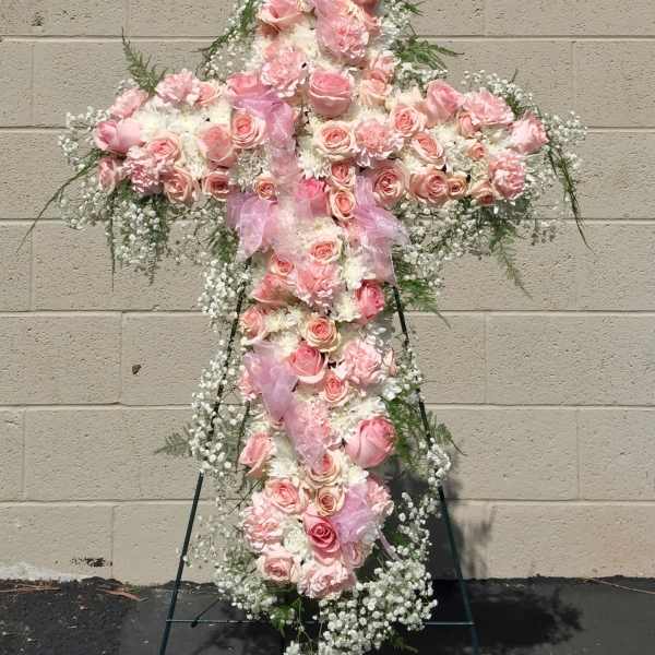 Pink floral cross on a stand with ribbon and white filler flowers