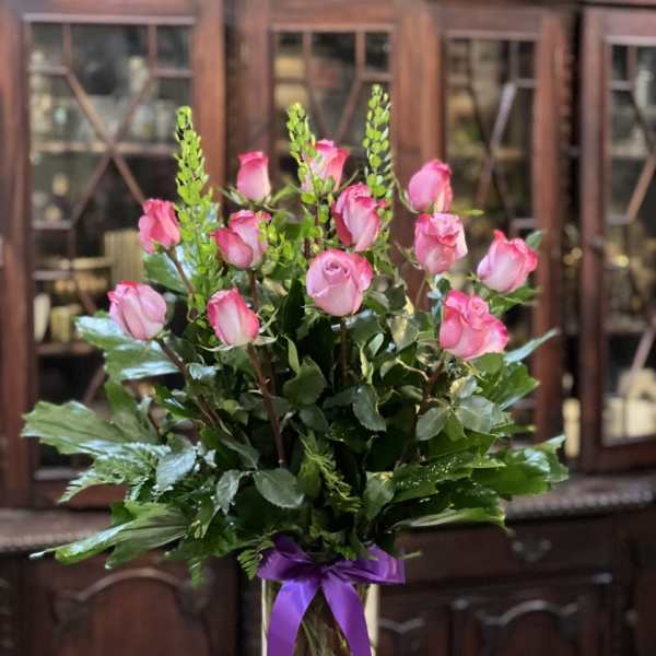 Pink roses in a clear glass vase with a purple ribbon