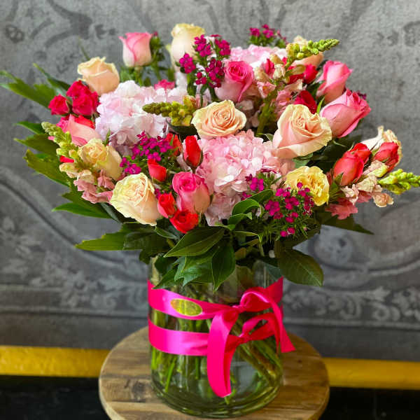 Mixed pink and cream roses in a glass vase with a pink ribbon